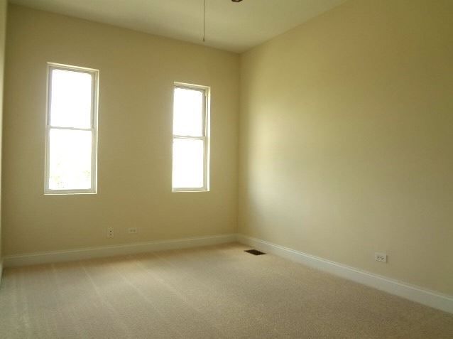 Empty beige-walled room with two tall windows and carpeted floor.