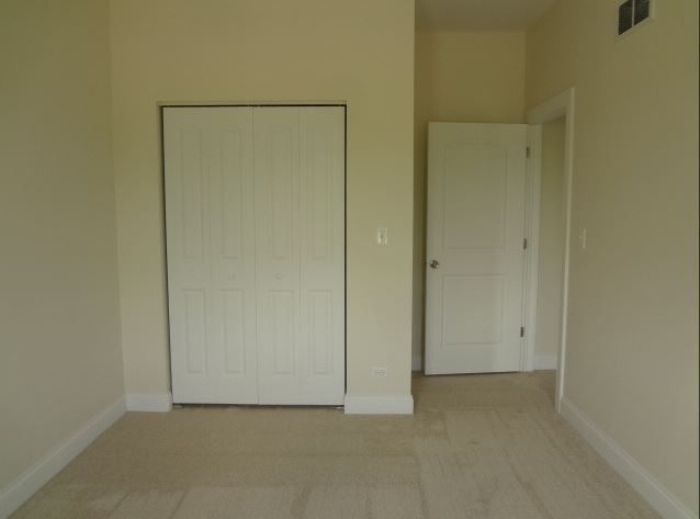 Empty room with beige walls, carpet, and closet. Doorway to another room visible.