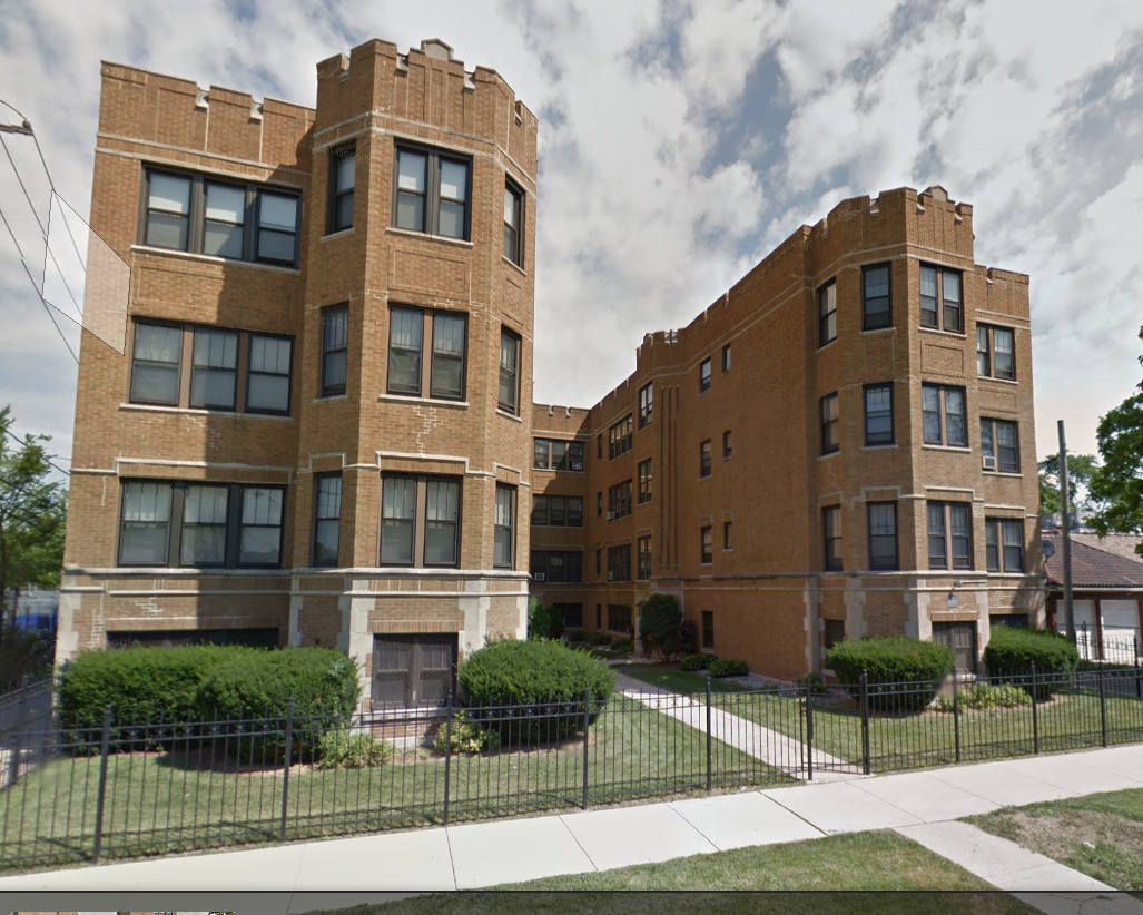 Multi-story brick apartment building with castle-like turrets and a black wrought-iron fence.
