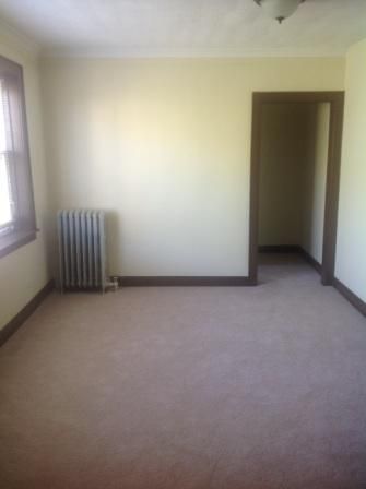 Empty room with beige walls, brown trim, carpet, and a radiator. Doorway visible.