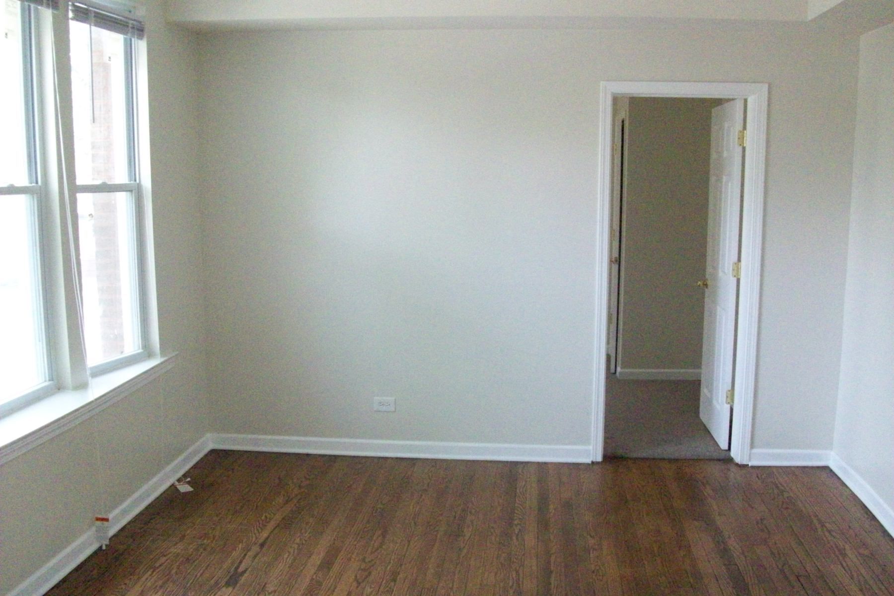 Empty room with hardwood floors, a window, and a doorway. Beige walls.