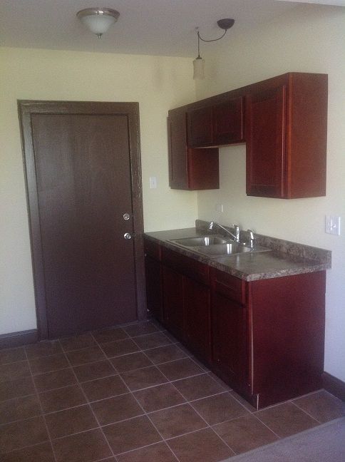 Kitchen with brown cabinets, sink, and door; brown tiled floor; tan walls.