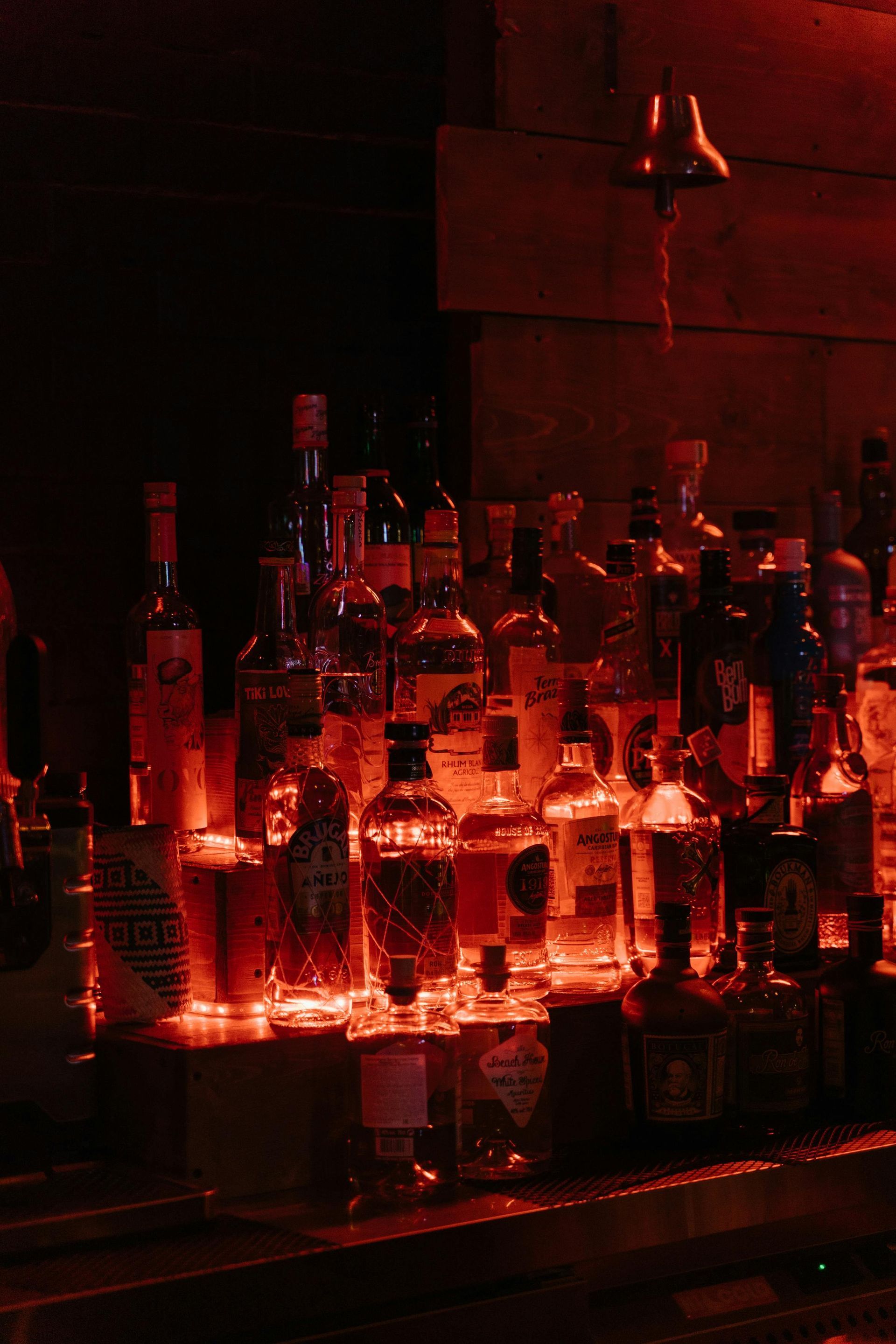 Shelves of various liquor bottles illuminated by dark red ambient lighting behind a bar.