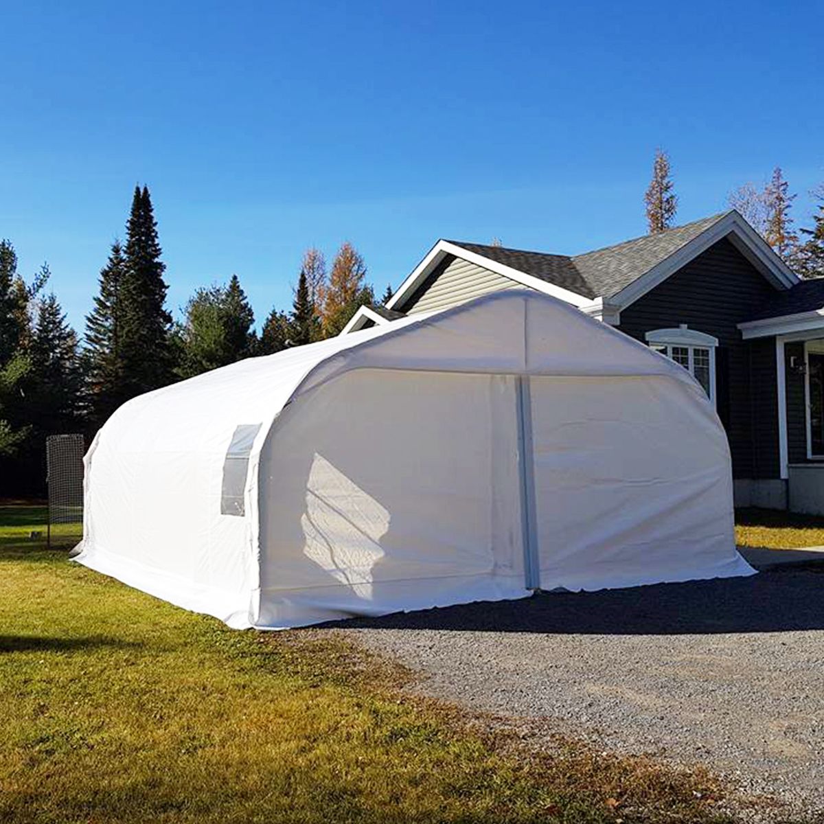 Bâtiment de stockage blanc à toit voûté dans une cour, près d'une maison, sur fond de ciel bleu.