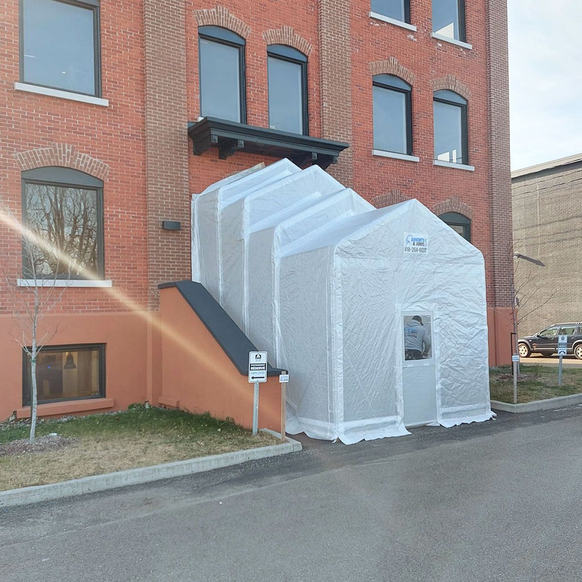 Extérieur d'un bâtiment en briques avec une structure blanche en forme de tente adossée à l'entrée.