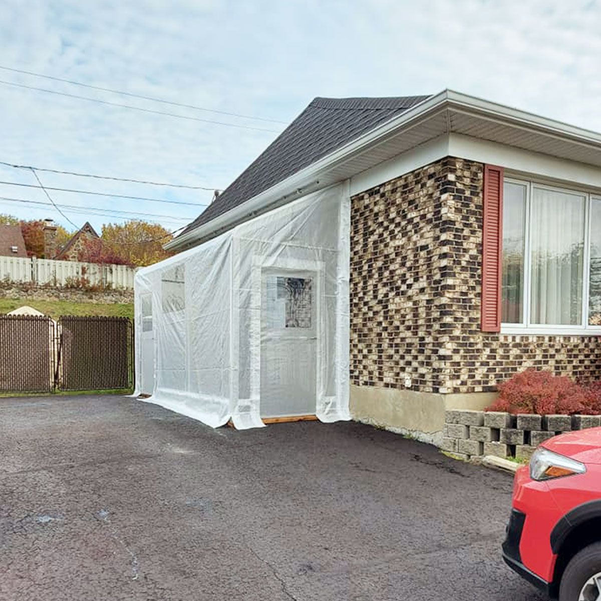 Un enclos en plastique blanc fixé à l'entrée d'une maison, avec une voiture garée à proximité.