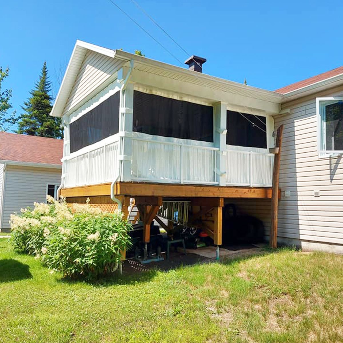 Véranda surélevée attenante à une maison aux boiseries blanches, au bardage beige et à la pelouse verte.