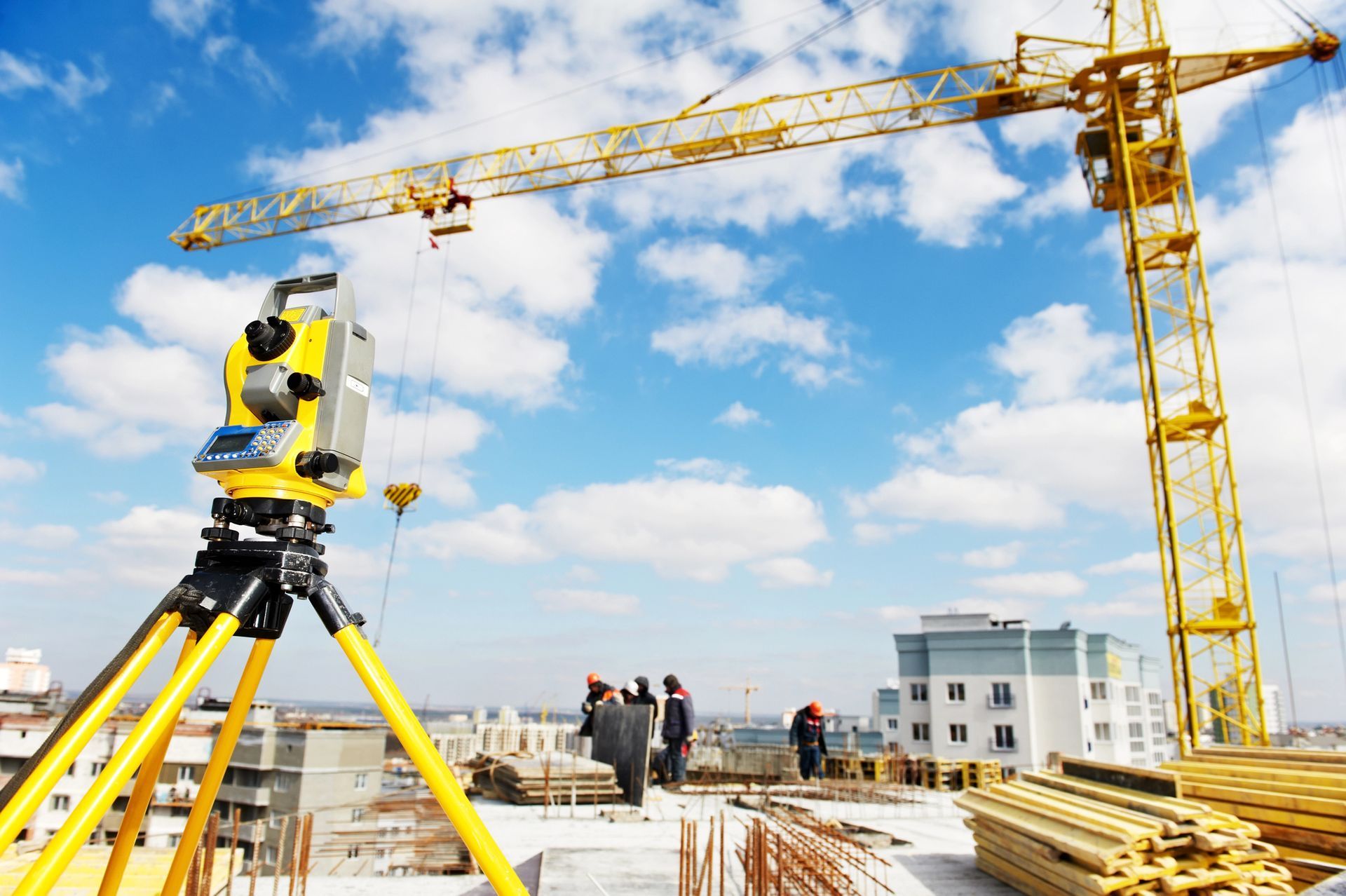 Equipo de topografía en el sitio de construcción con trabajadores, grúa y edificios contra un cielo azul.