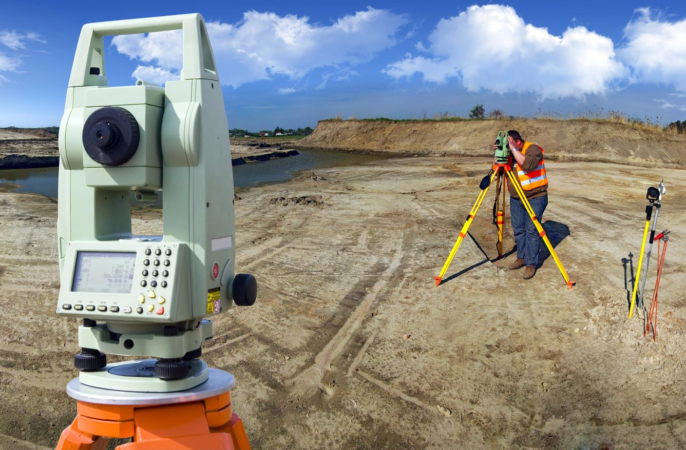Agrimensor utilizando un teodolito en el sitio de construcción, midiendo el terreno con instrumentos.