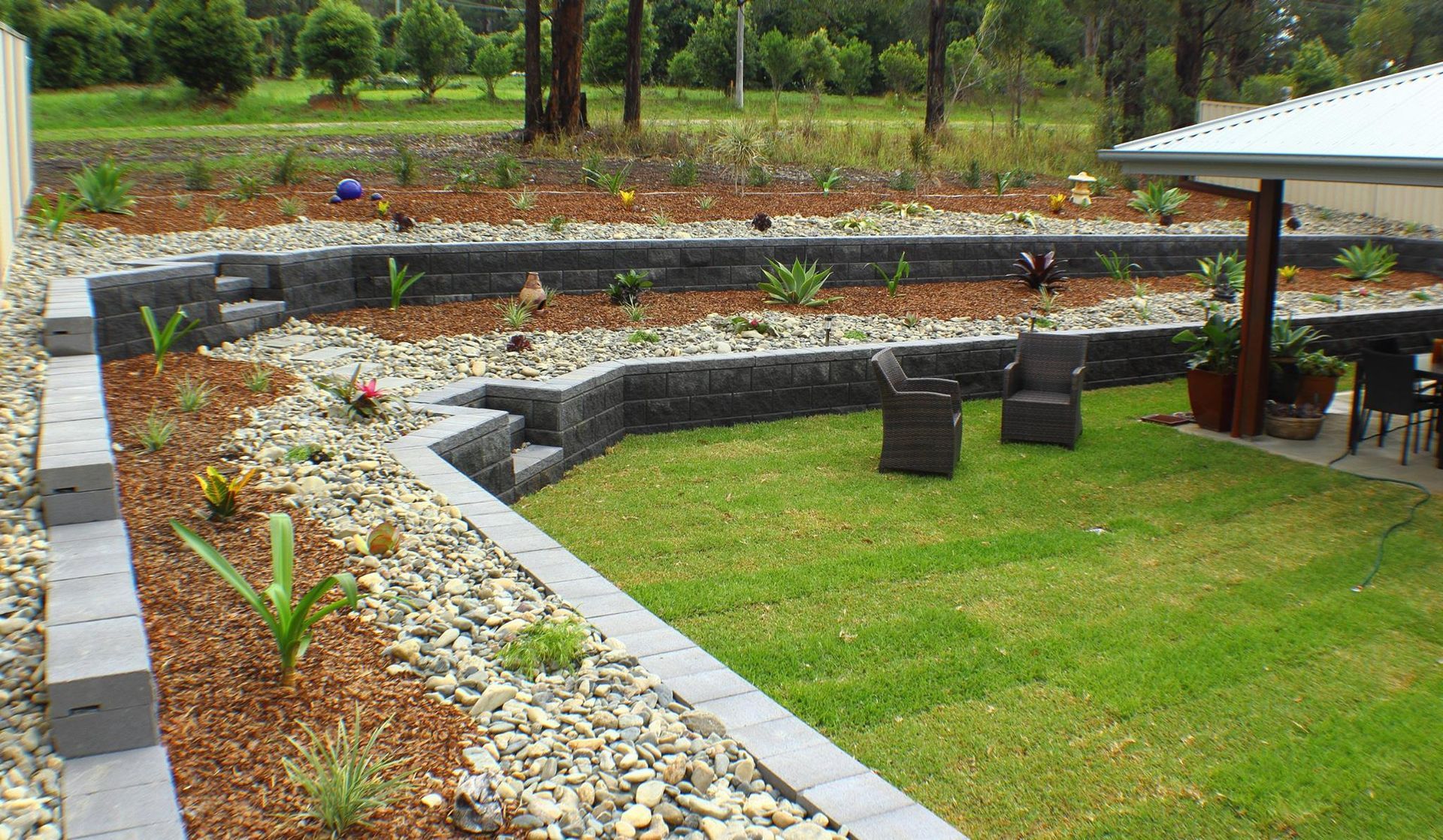 A Lush Green Lawn With a Stone Wall and Chairs — Seascapes Landscape Construction in Kendall, NSW