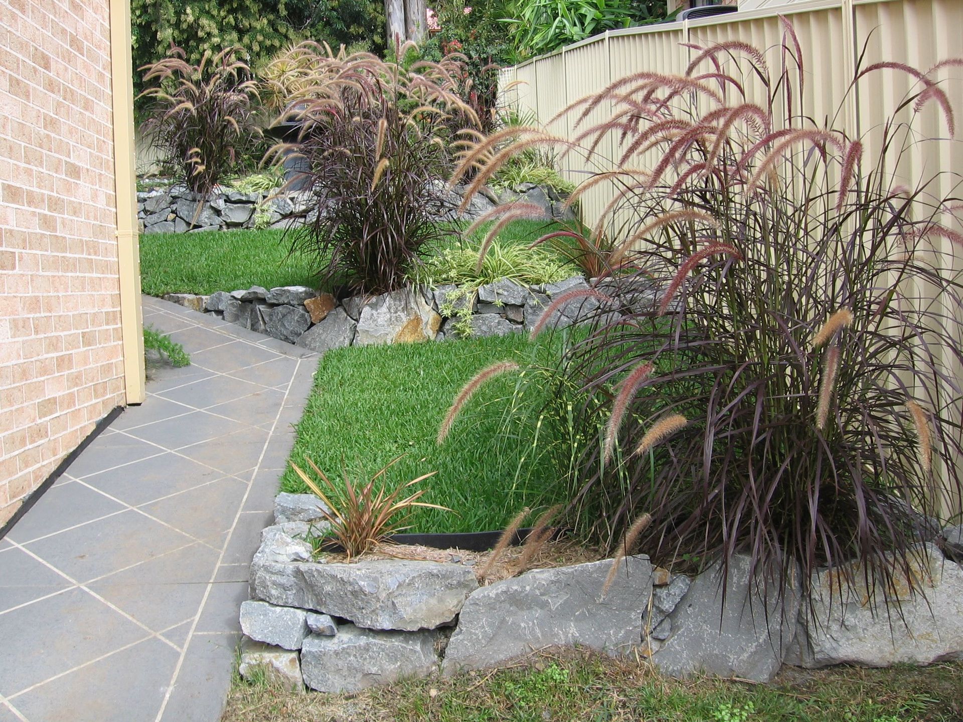 A Stone Wall Surrounds a Lush Green Lawn in a Backyard — Seascapes Landscape Construction in Kendall, NSW