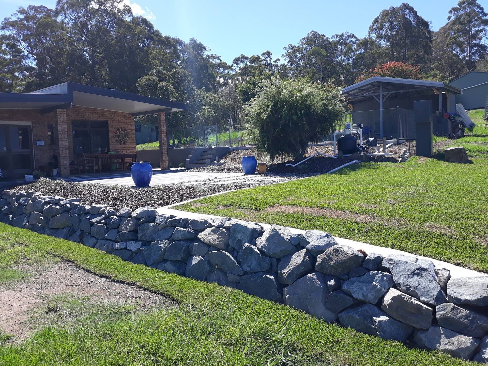 A Stone Wall Surrounds a Lush Green Lawn in Front of a House — Seascapes Landscape Construction in Kendall, NSW