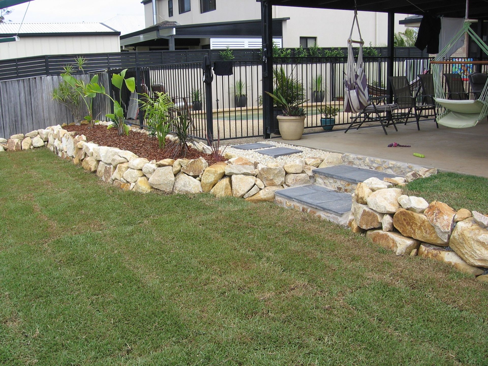 A Backyard With a Stone Wall and a Fence — Seascapes Landscape Construction in Kendall, NSW