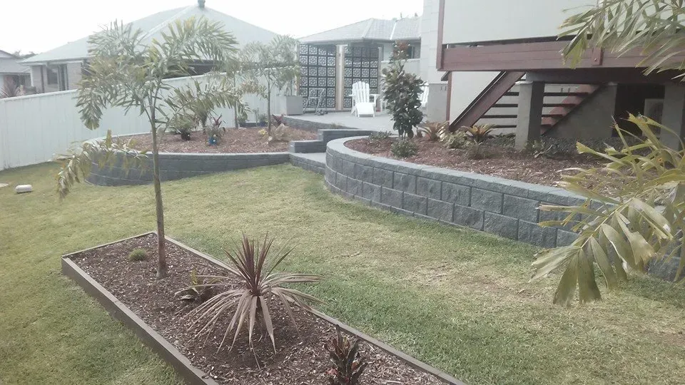 A Lush Green Lawn in Front of a House With a Brick Wall Surrounding It — Seascapes Landscape Construction in Kendall, NSW
