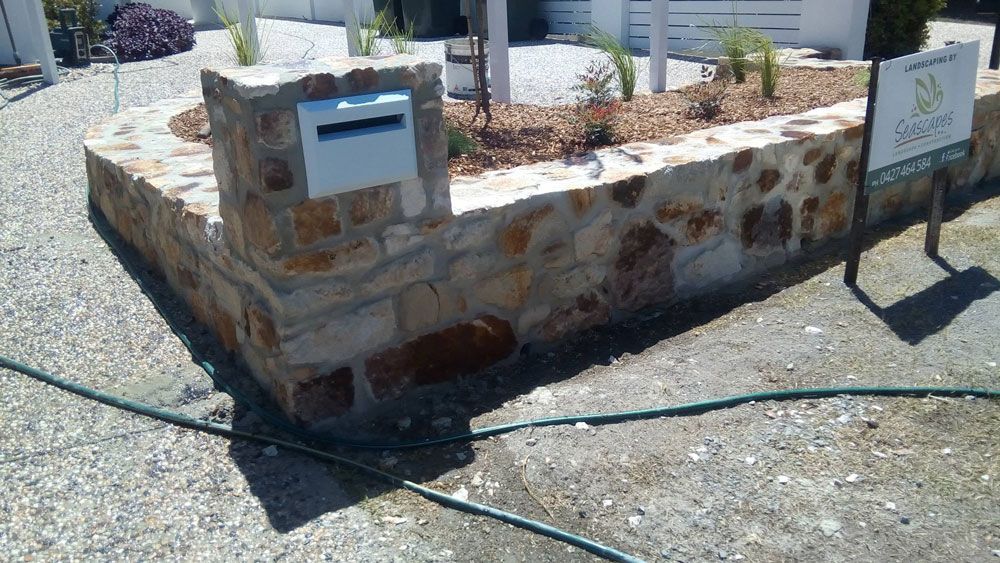 A Stone Wall With a Mailbox and a Sign on It — Seascapes Landscape Construction in Kendall, NSW