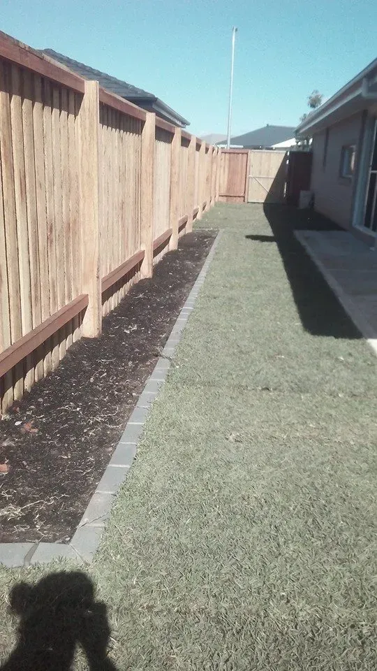 A Wooden Fence Surrounds a Lush Green Lawn in a Backyard — Seascapes Landscape Construction in Laurieton, NSW