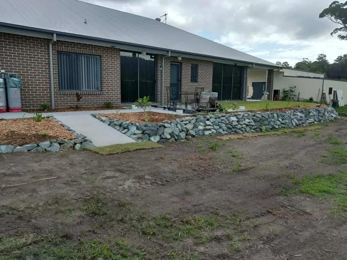 A Large Brick House With a Stone Wall in Front of It — Seascapes Landscape Construction in Kendall, NSW