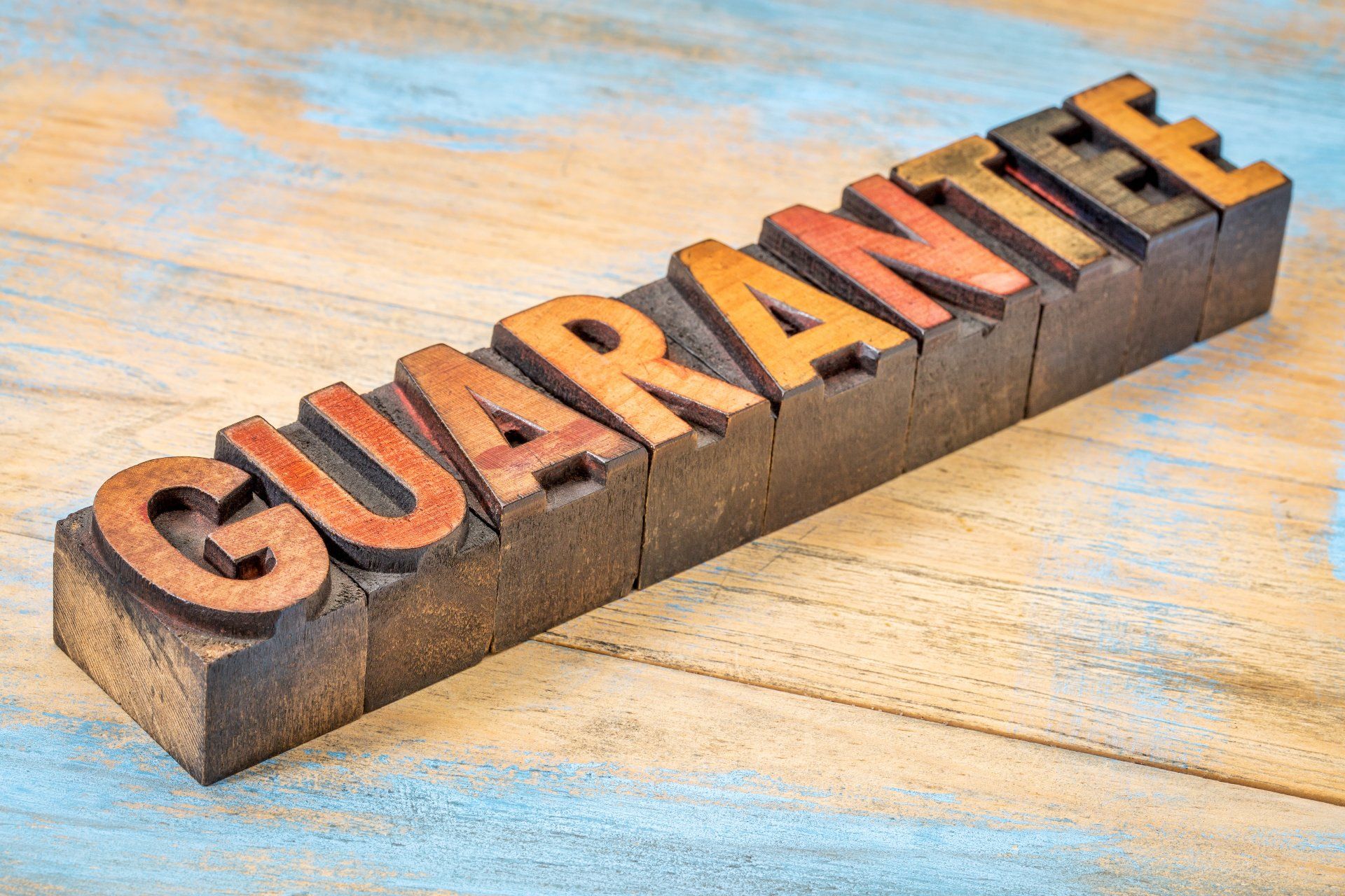 The word guarantee is written in wooden letterpress type on a wooden table.