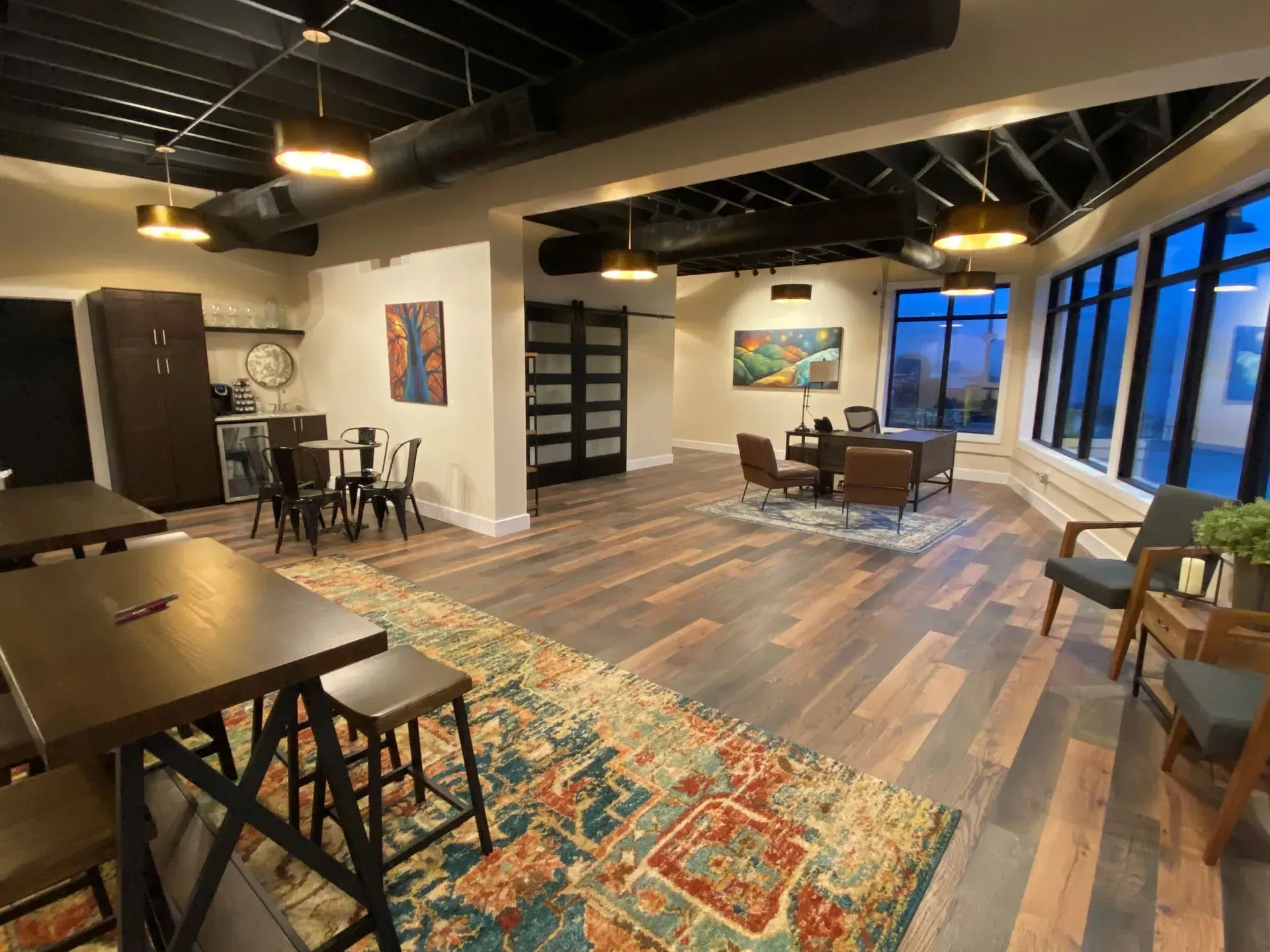 Modern open-concept loft with dining table, rugs, lounge chairs, and large windows overlooking a city view