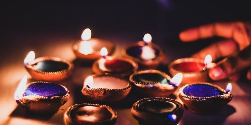 Rows of glowing oil lamps with blue and orange flames in a dark setting