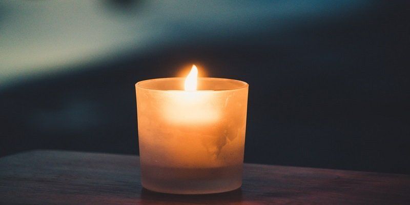 Lit candle glowing on a dark surface in a dim, blurred setting