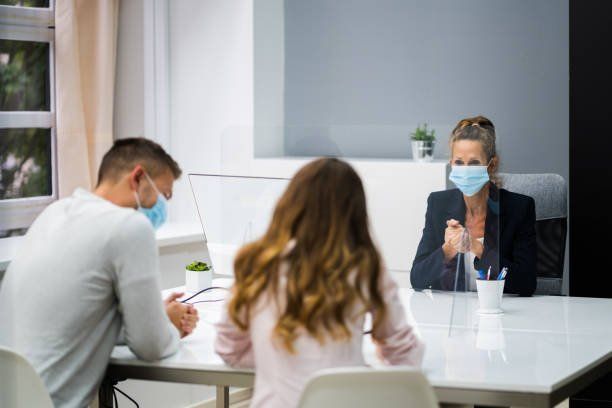 Masked people in a meeting room talking across a white table