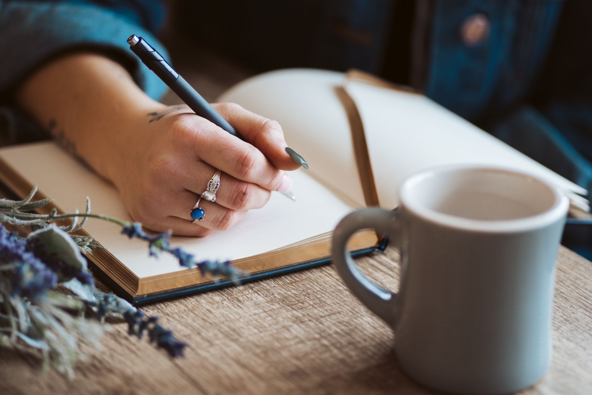 Hand writing in an open notebook beside a coffee mug on a wooden table