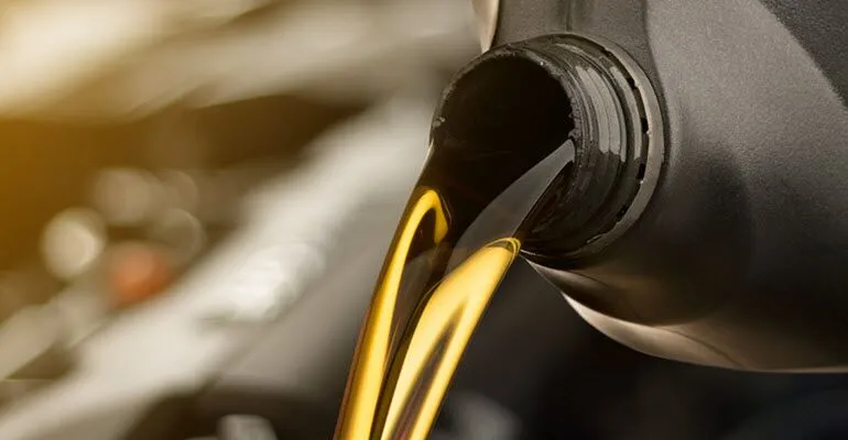 A close up of a bottle of oil being poured into a car engine.