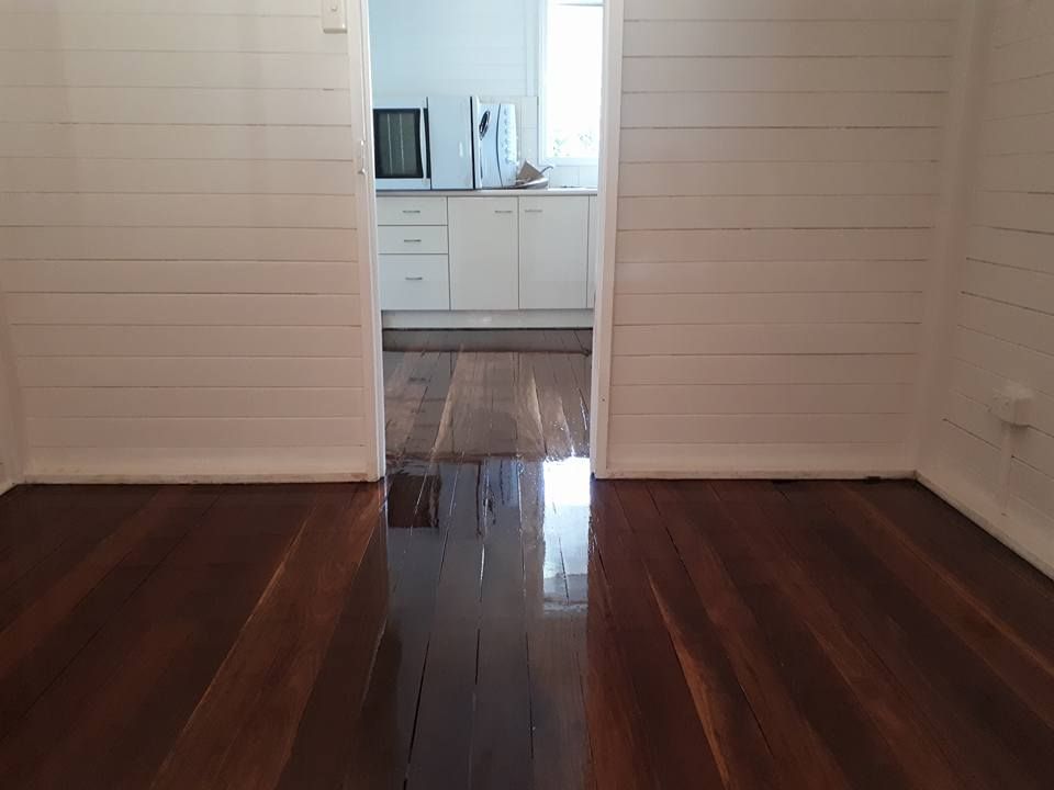 An Empty Room with Wooden Floors and White Walls Leading to A Kitchen — Finish It Floor Sanding in Bucca, QLD