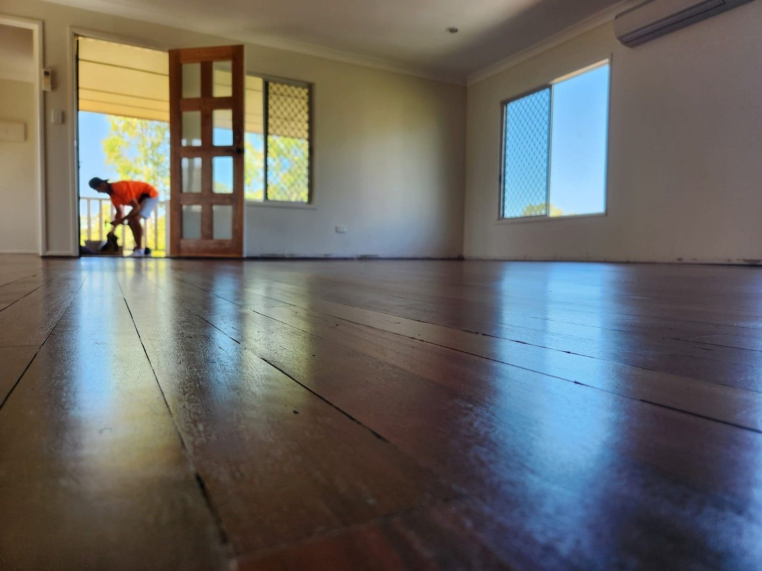 A Man Is Bending Over in An Empty Room with A Wooden Floor — Finish It Floor Sanding in Bucca, QLD