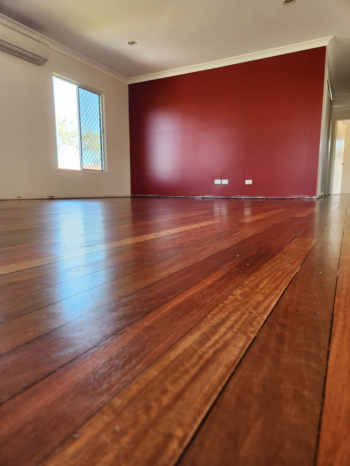 An Empty Room with A Wooden Floor and A Red Wall — Finish It Floor Sanding in Bucca, QLD