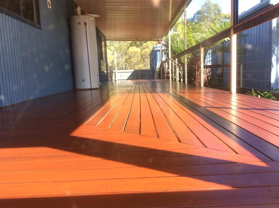 A Wooden Deck with A Blue Building in The Background — Finish It Floor Sanding in Bucca, QLD