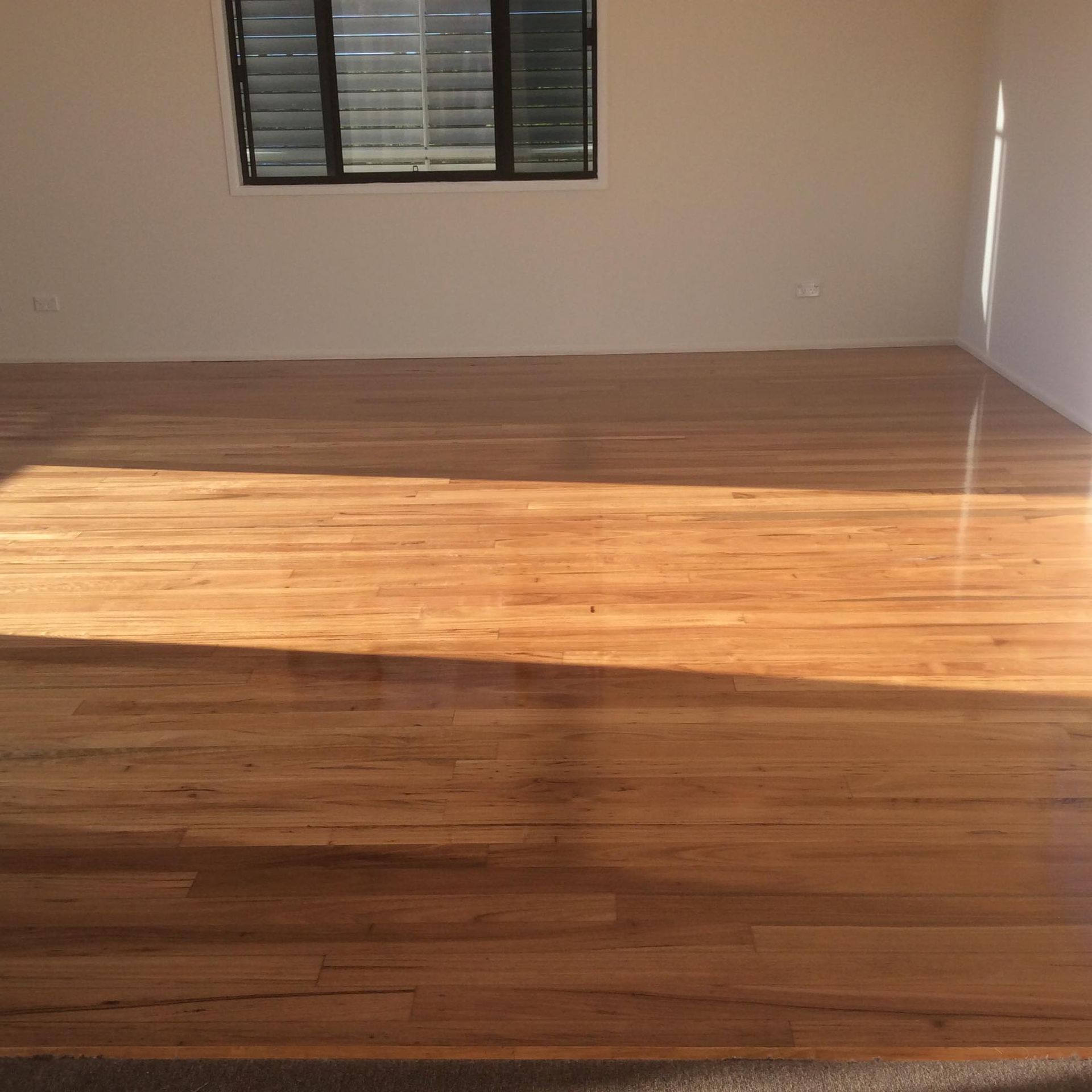 An Empty Room with A Wooden Floor and A Window — Finish It Floor Sanding in Bucca, QLD