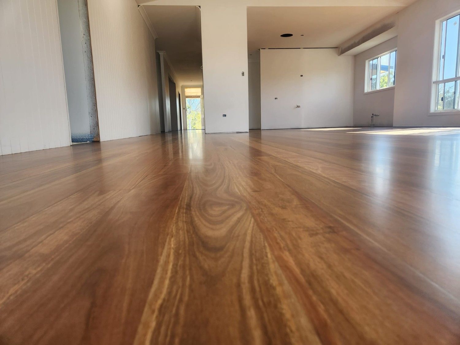 A Large Empty Room with A Wooden Floor and White Walls — Finish It Floor Sanding in Gladstone, QLD