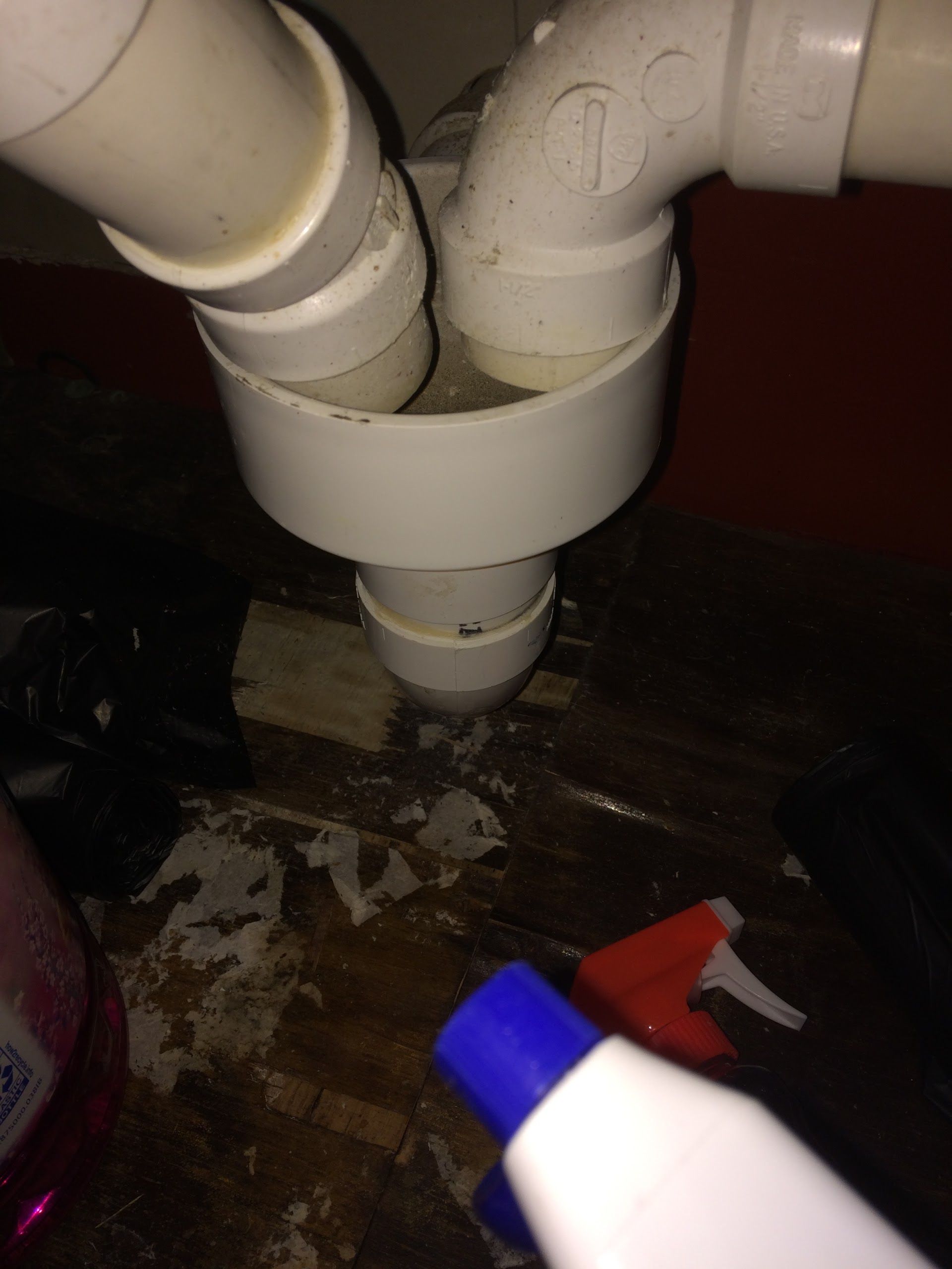 A high-angle view shows two white PVC drain pipes emptying into a central white funnel-shaped drain trap under a sink.