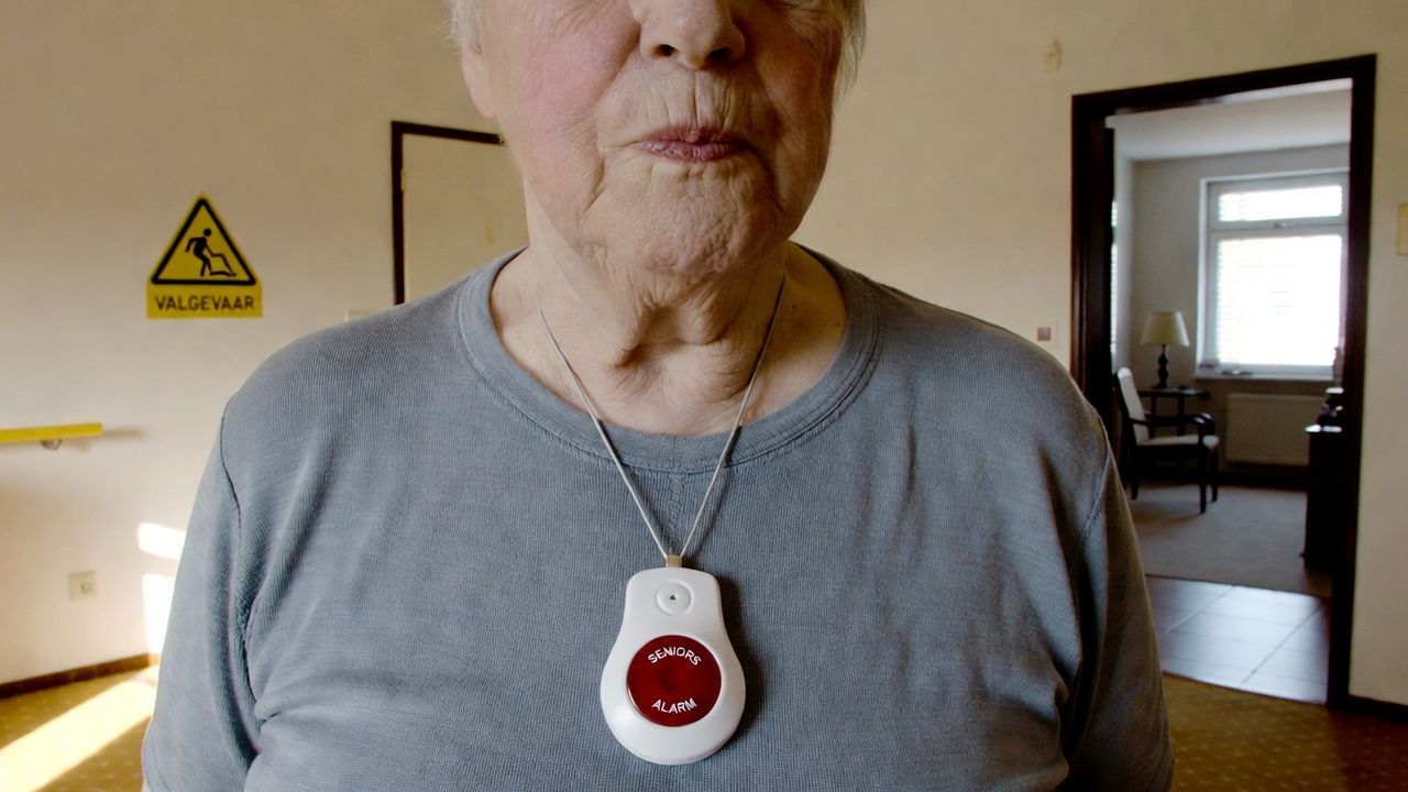 Oudere vrouw draagt een alarmknop om de nek in een veilige thuisomgeving