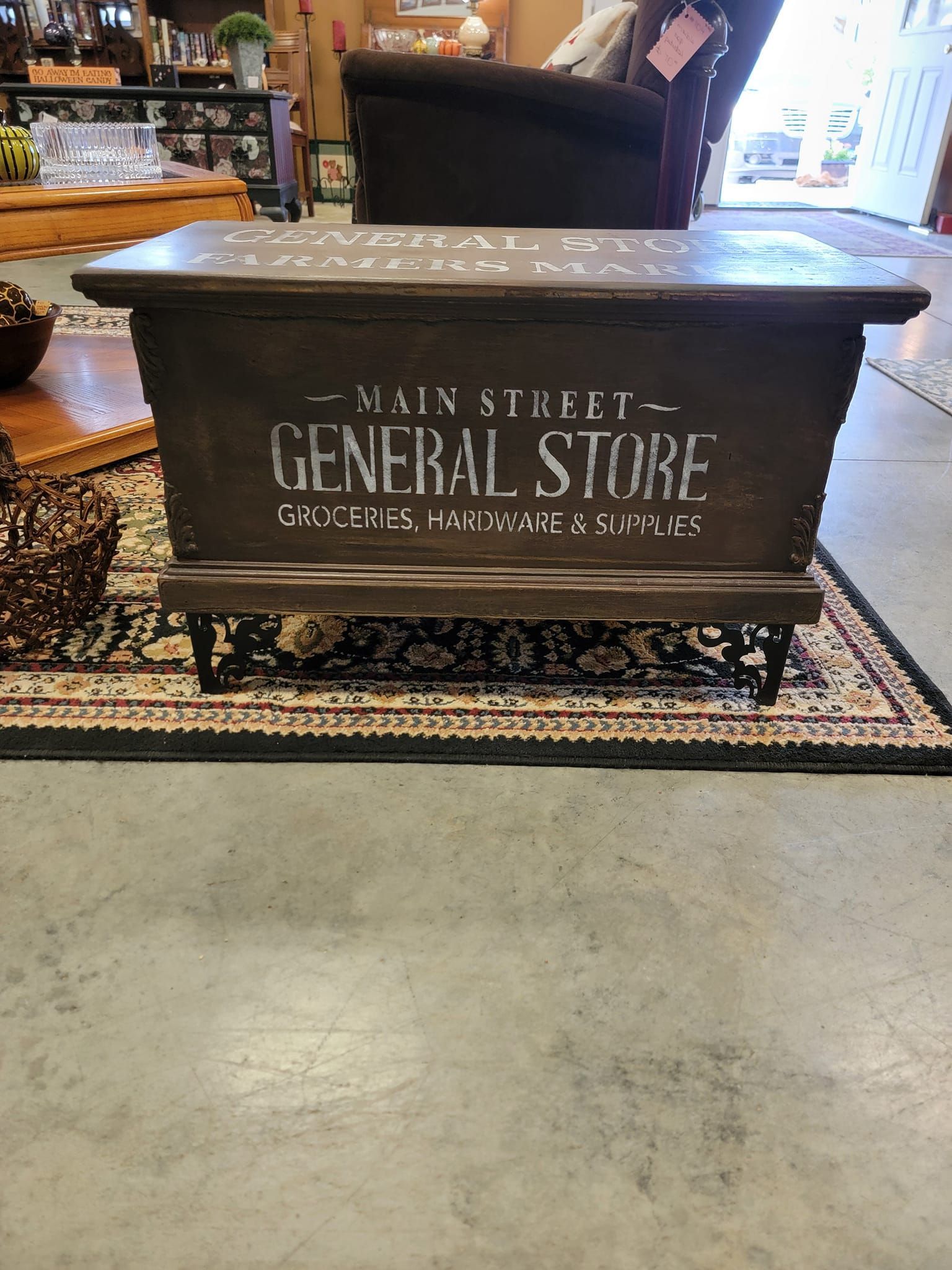 A trunk with the word general store painted on it is sitting on a rug in a living room.