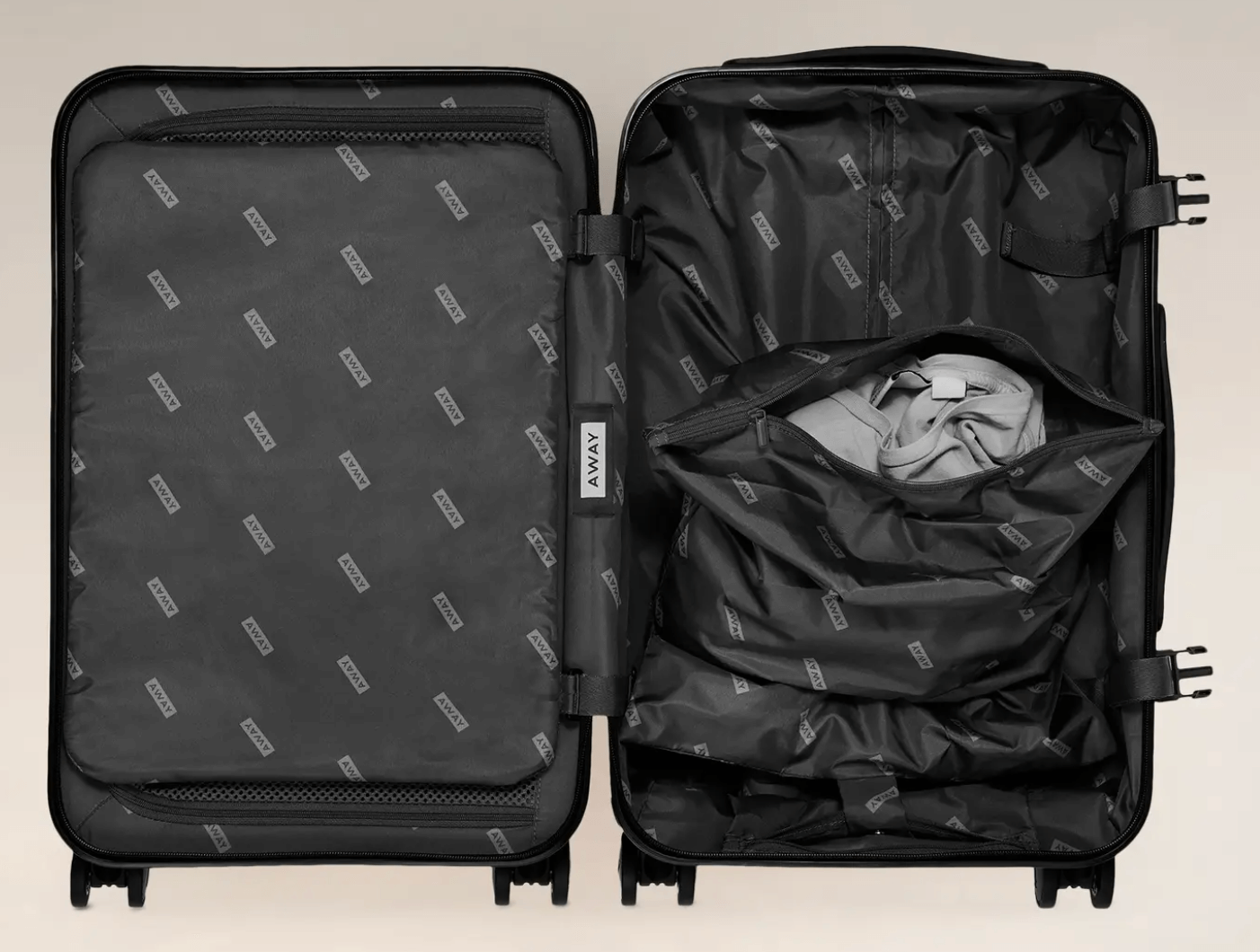 away bigger carry on open suitcase black interior with away logo design black away logo laundry bag with grey clothing inside black wheels on bottom of suitcase