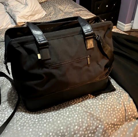 beis the convertible weekender bag packed bag black leather straps on gray bedspread black coat black nightstand