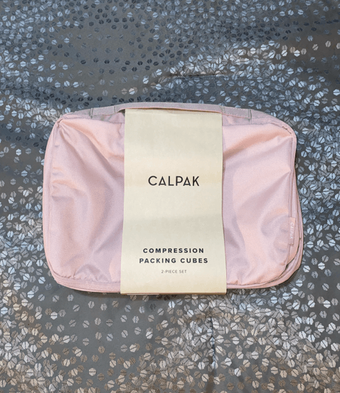 calpak compression packing cube set pink sand color on gray patterned bedspread with tan calpak label