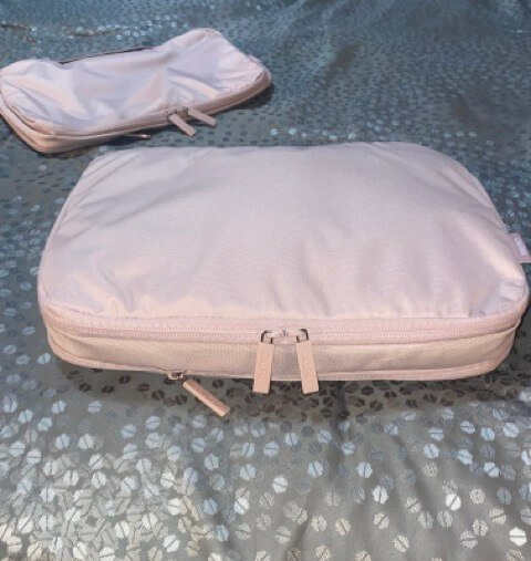 calpak pink packing cube with clothing fully zipped and compressed on gray bedspread with additional empty pink packing cube in background