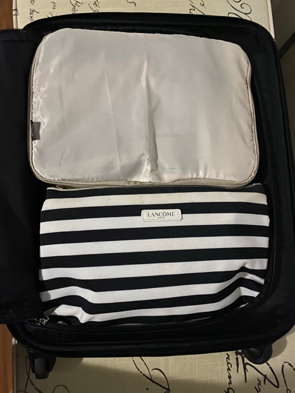 cream zipped packing cube in suitcase, lancome black and white striped toiletry organizer