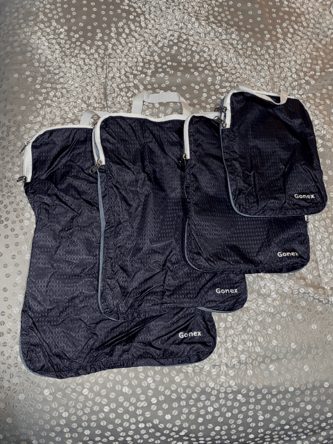 gonex black compression packing cubes set of four cubes with gray gonex text gray zipper gray top handles on patterned gray bedspread