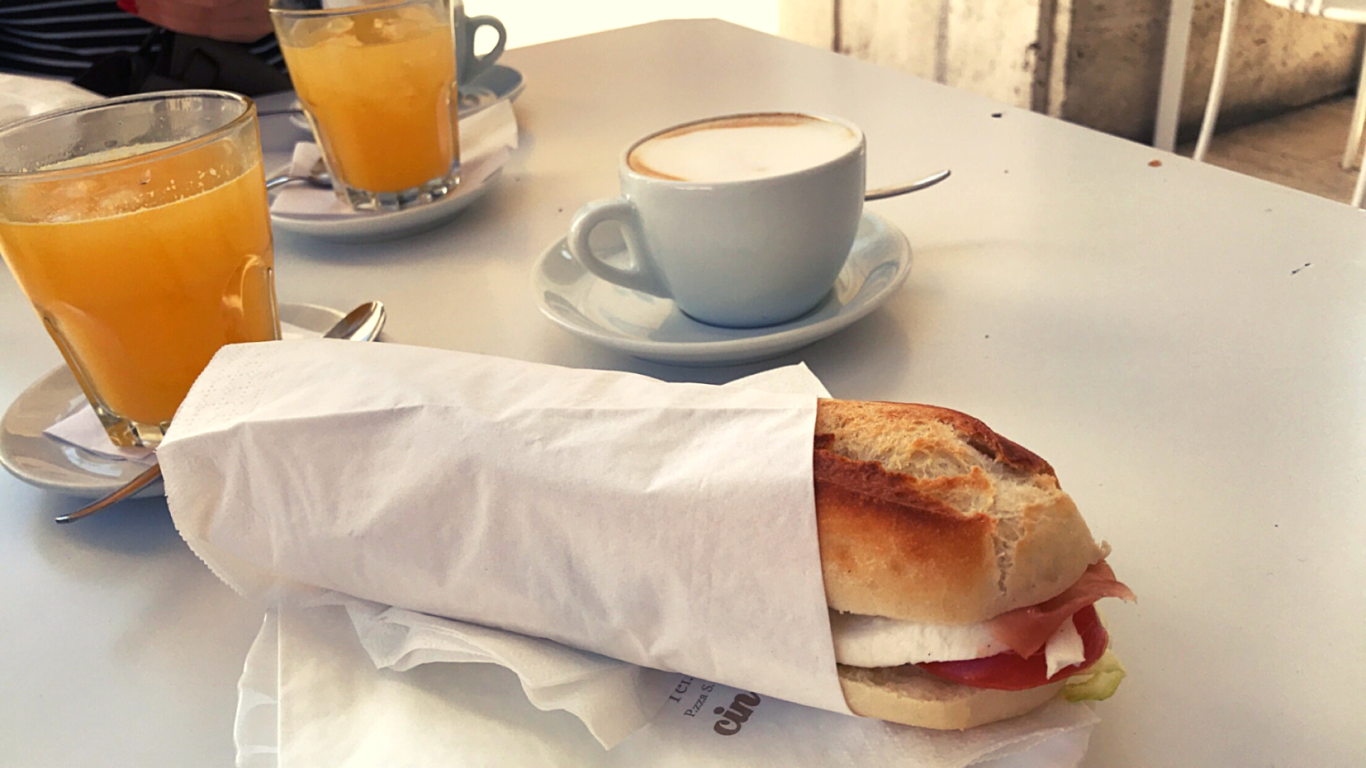 breakfast sandwich tomato mozzarella orange juice cups cappuccino coffee white table