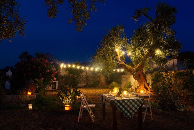 Masseria Il Frantoio Puglia Italy backyard picnic at night string lights trees white chairs wooden table checkered tablecloth