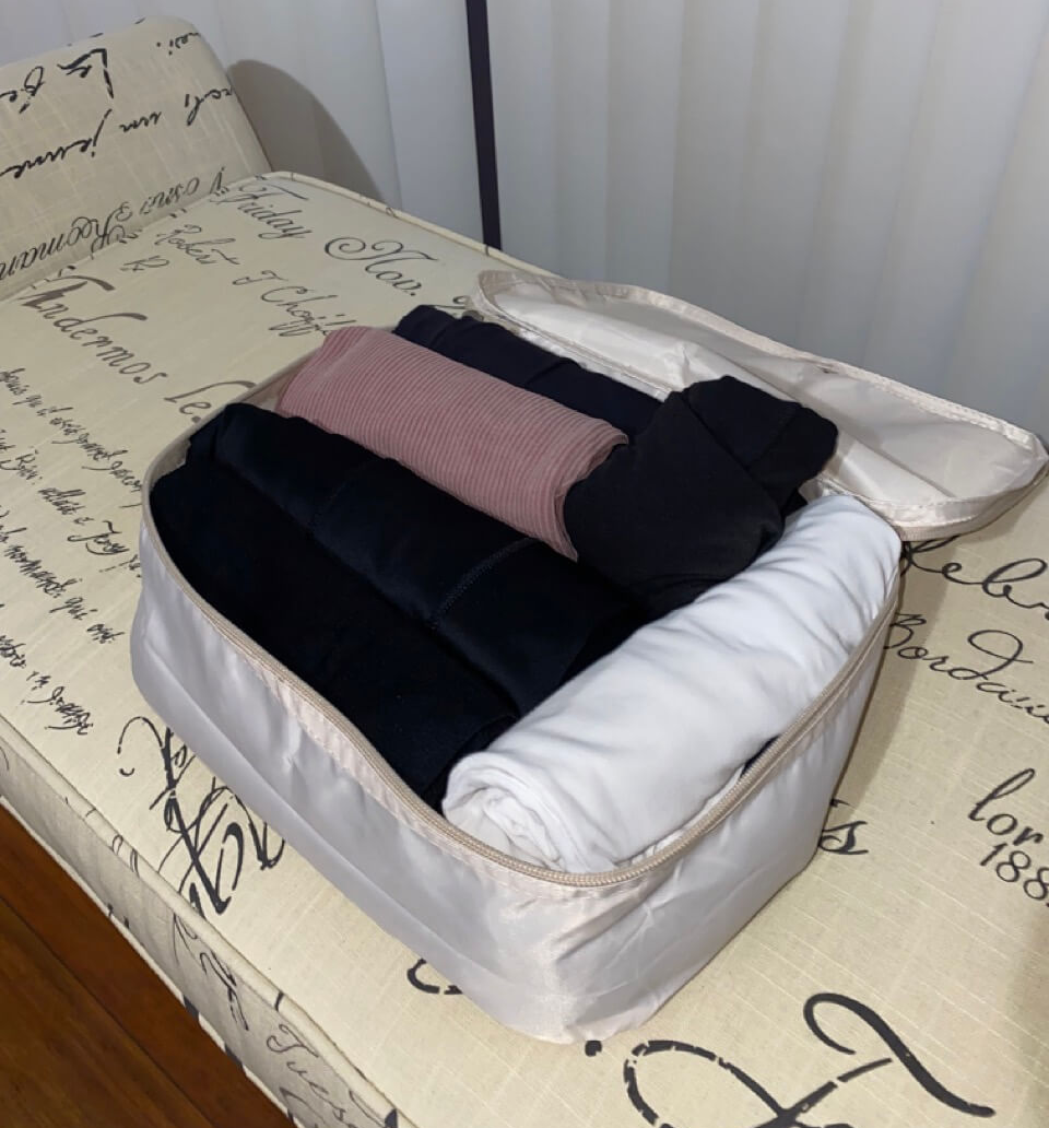 beige packing cube unzipped with white pink and black rolled clothes on a tan bench with brown lettering