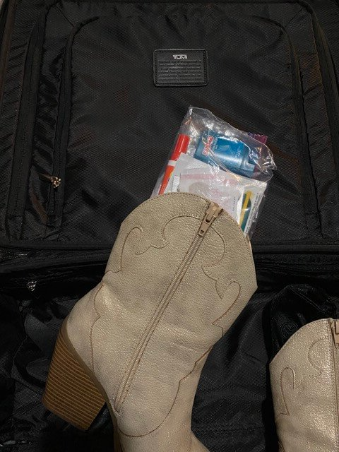 tan cowboy boots inside black tumi suitcase with plastic bag with bandaids and antibiotic cream stored inside