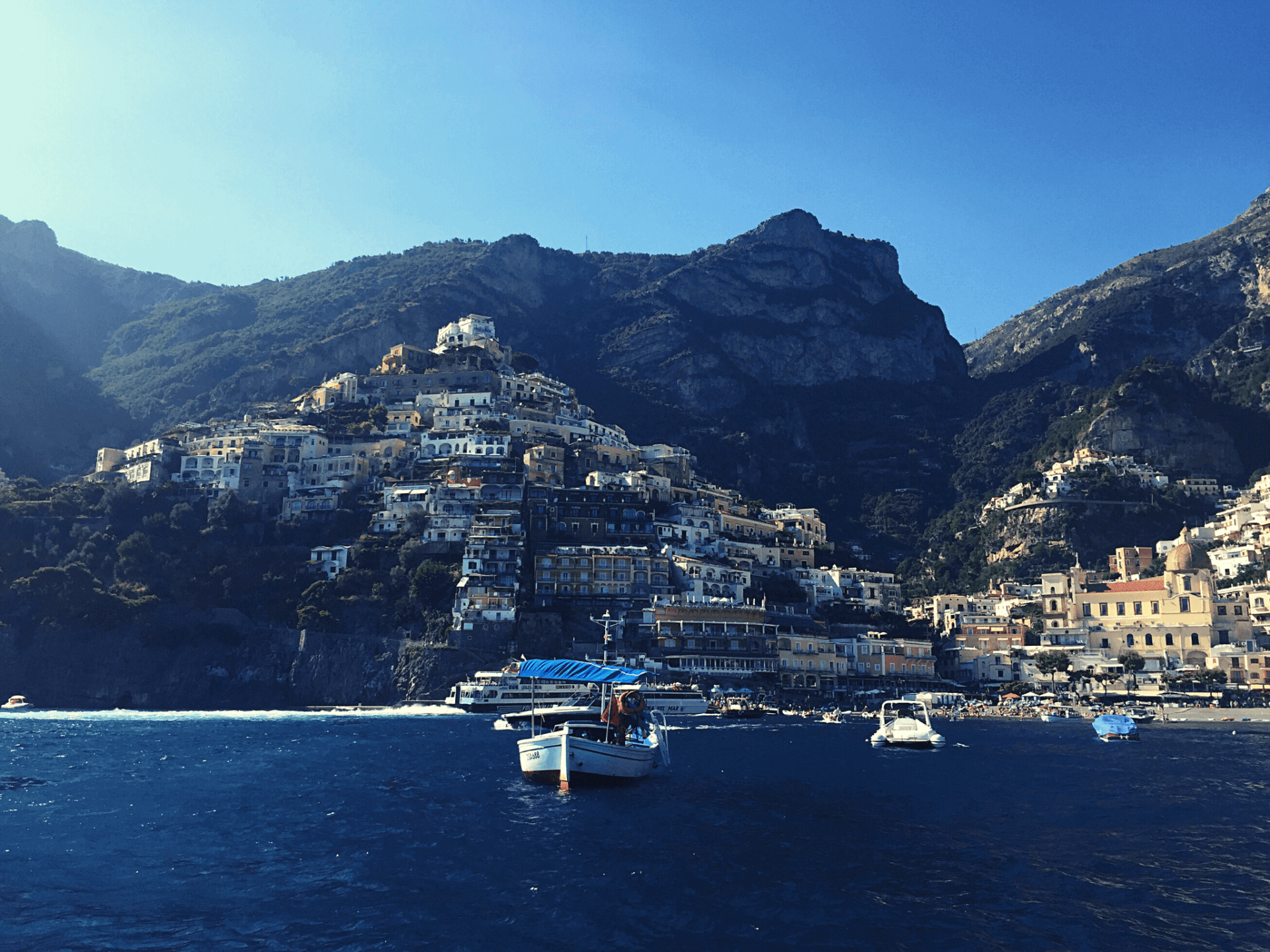 positano italy water with boats cliffs in background white and tan buildings