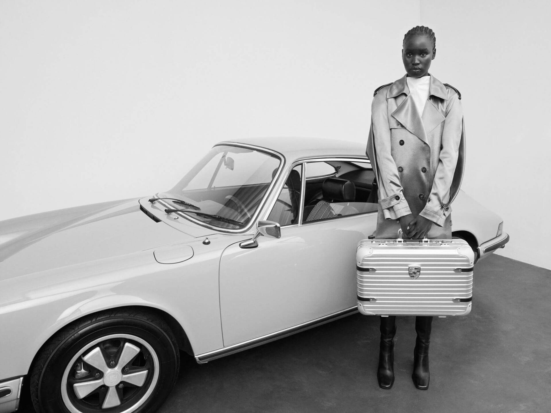 rimowa porsche collaboration suitcase black and white photo woman holding suitcase in front of porsche 911 car