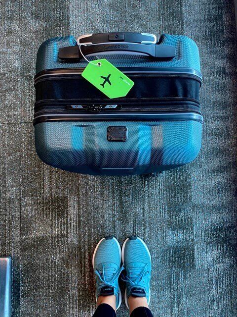 teal green samsonite carry on bag top view expanded, lime green luggage tag with black plane logo, green adidas sneakers